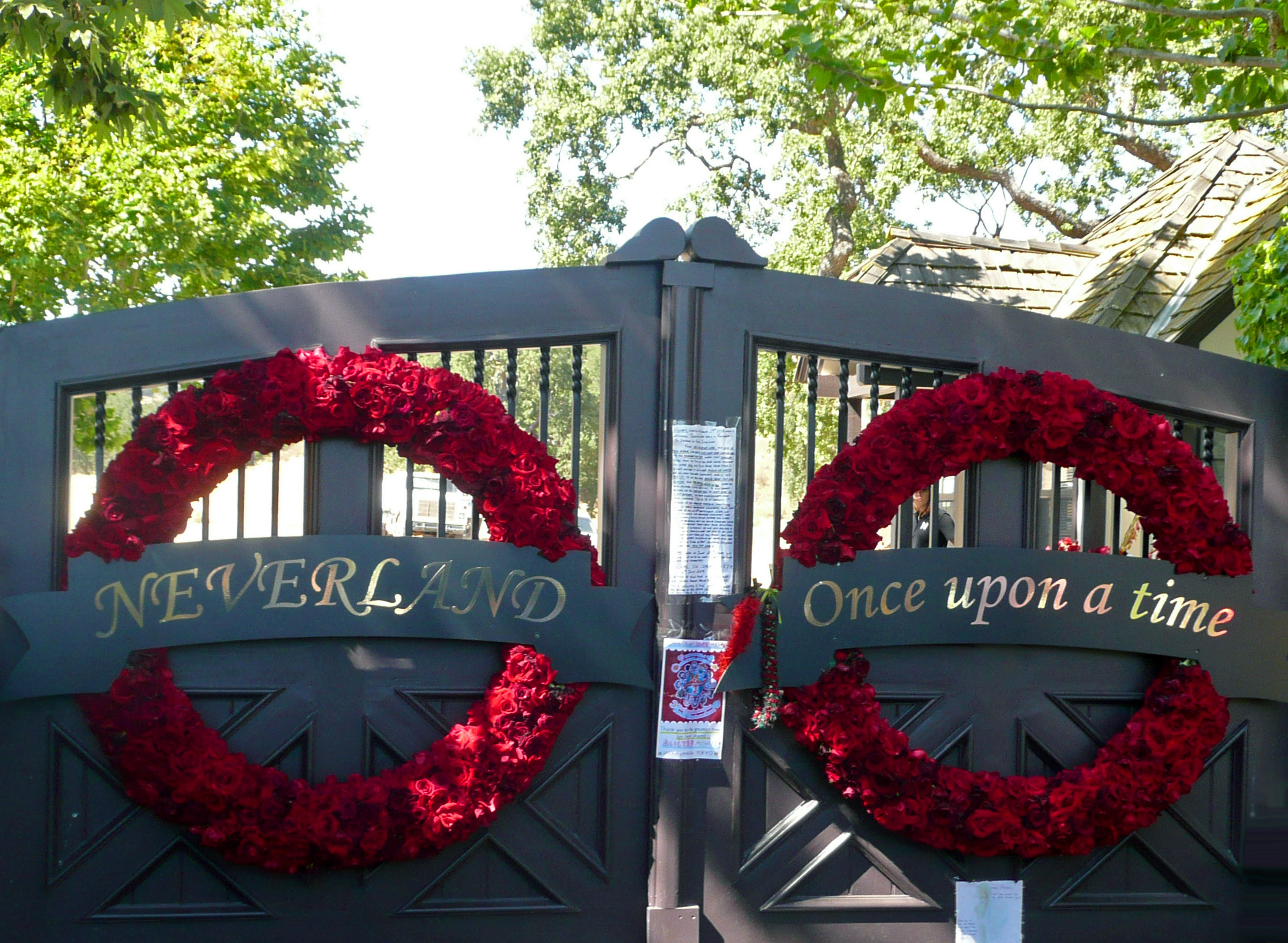 The Neverland Ranch gates with the lettering 'Neverland — Once upon a time' and red floral wreaths